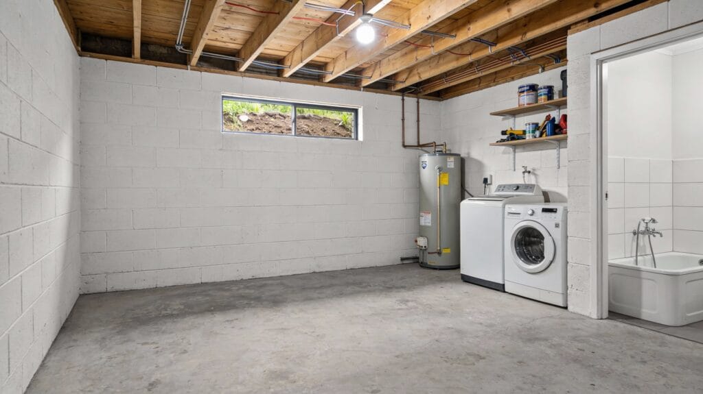 Musty, cluttered Auckland garage interior with visible damp patches on the concrete wall, illustrating the source of a musty odour and early signs of moisture problems.