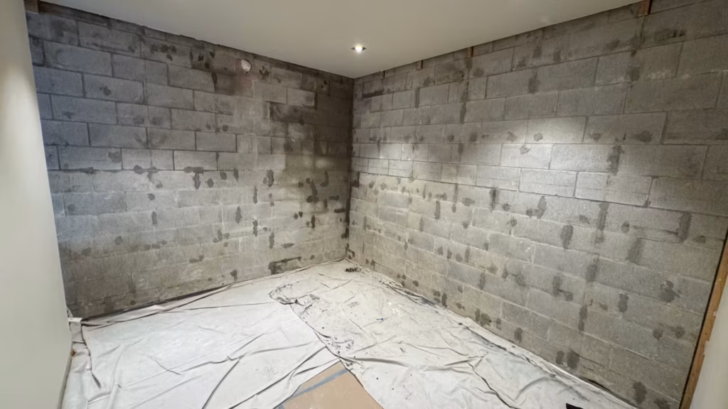Bare concrete block basement wall in Parnell with linings removed, showing dark wet patches and damp areas before internal waterproofing.